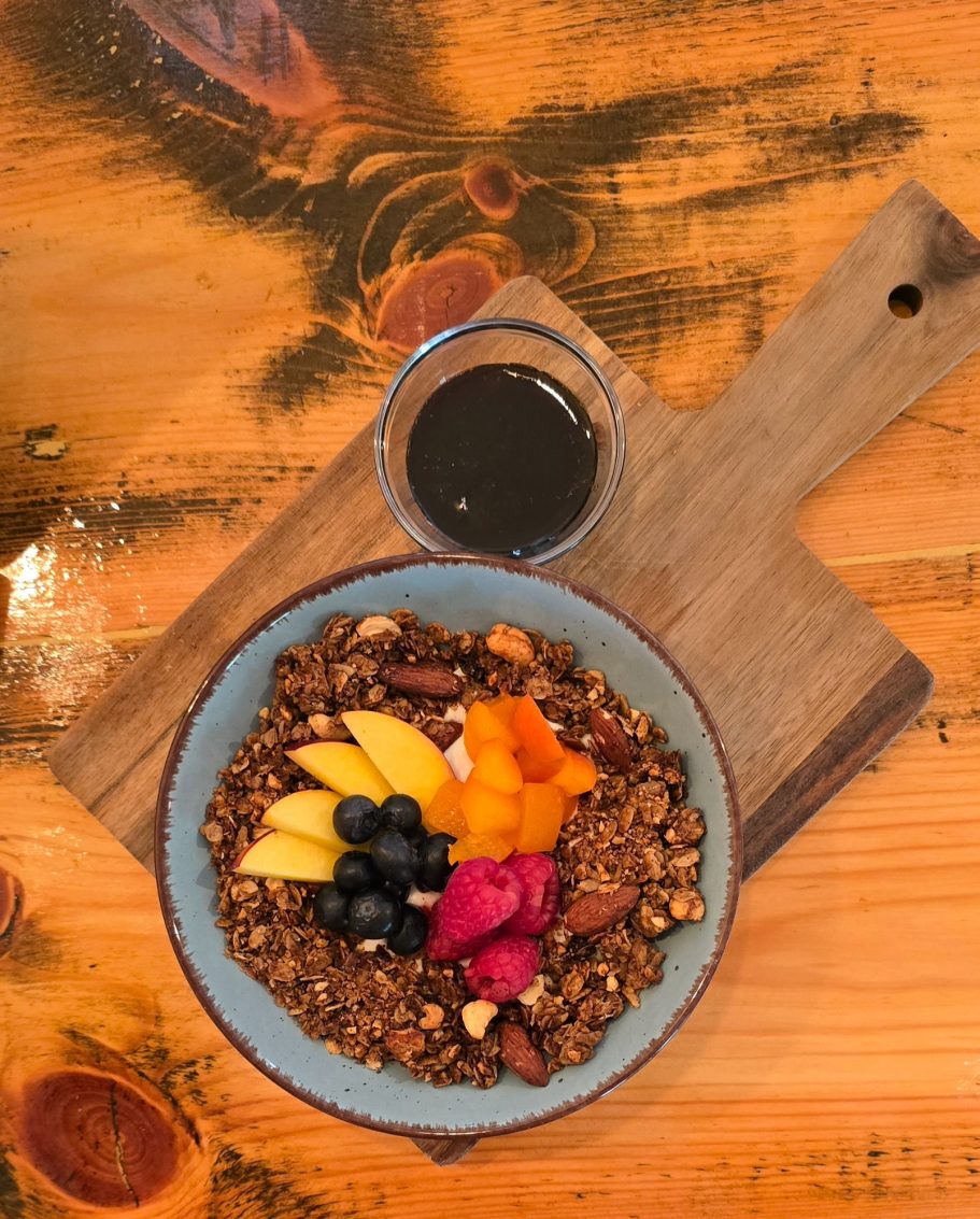 fresh´n healthy Schale mit Granola, frischen Früchten und einem kleinen Glas Sirup auf einem Holztisch.