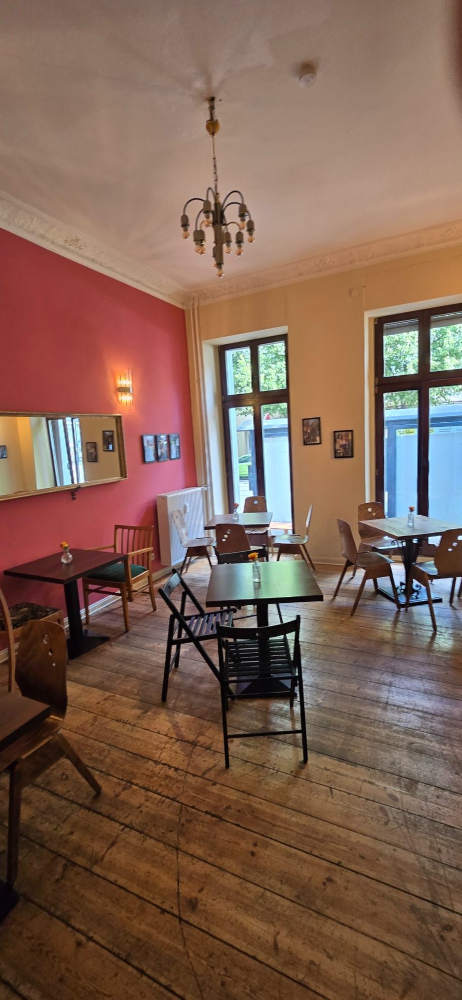 Blick in den 2. Gastraum Gemütlicher Raum mit Tischen, Stühlen und großen Fenstern, Holzfußboden und bunten Wänden.