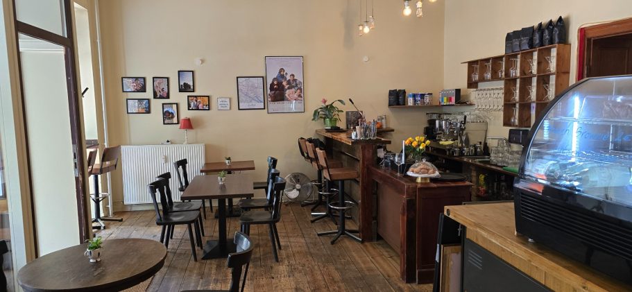 Blick in den 1. Gastraum Gemütliches Café mit Tischen, einer Theke und Bildern an der Wand.